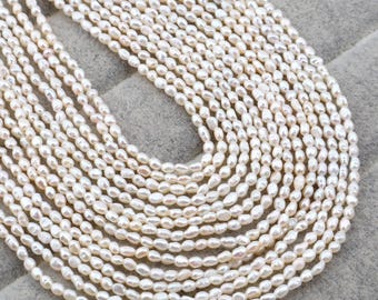 May include: A collection of creamy white, oval-shaped pearls, strung together in multiple strands. The pearls have a natural luster and are arranged in a layered pattern, creating a full and textured appearance. The background is a neutral gray.