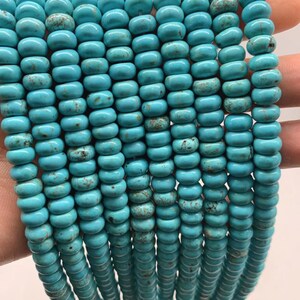 May include: A strand of turquoise beads, each bead is a light blue color with brown speckles and a slightly rounded shape.