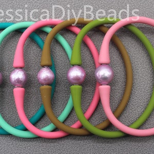 May include: Six colorful silicone bracelets with a single pink pearl bead on each. The bracelets are teal, mint green, pink, brown, green, and pink.