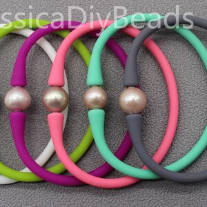 May include: Six silicone bracelets with a single pearl bead in the center of each bracelet. The bracelets are in the colors white, green, pink, purple, gray, and teal.