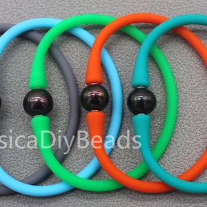 May include: Five silicone bracelets with black pearl accents. The bracelets are in the colors gray, blue, green, orange, and teal.