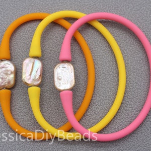 May include: Three silicone bracelets with a pearl accent. The bracelets are orange, yellow, and pink.