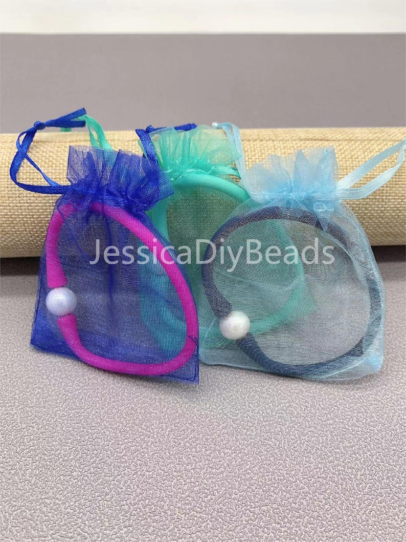 May include: Three small organza bags with drawstrings, each containing a hair tie and a pearl bead. The bags are blue, teal, and pink.