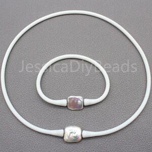 May include: A set of two white silicone necklaces with square pearl beads. The necklace on the left is longer than the necklace on the right.
