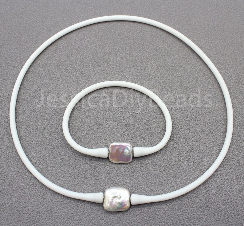 May include: A set of two white silicone necklaces with square pearl beads. The necklace on the left is longer than the necklace on the right.