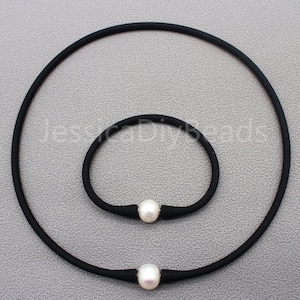 May include: A set of two black elastic necklaces with a single white pearl accent on each. The necklace on the left is longer than the necklace on the right.