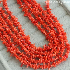 Peut inclure: Un brin de perles de corail rouge vif, chaque perle est de forme longue, mince et irrégulière. Les perles sont disposées en un motif lâche et fluide.