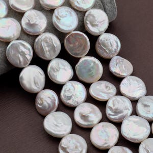 May include: A collection of lustrous, white coin-shaped pearls. The pearls have a smooth, iridescent surface with subtle variations in color. The pearls are arranged closely together, suggesting they are part of a larger strand or collection, perfect for jewelry making.