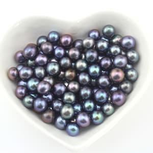 May include: A heart-shaped bowl filled with iridescent black pearls. The pearls have a blue and purple sheen.