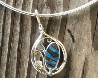May include: A silver pendant with a blue, green, and brown stone set in a silver wire frame. The pendant is hanging from a silver chain.
