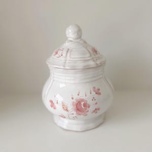 May include: White ceramic sugar bowl with a lid, featuring a pink floral design. The lid has a knob on top.