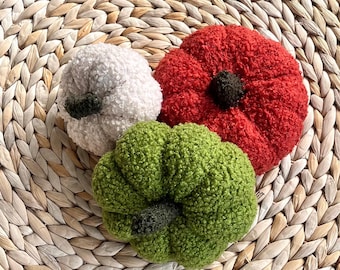 May include: Three plush pumpkin-shaped decorations made of textured, curly fabric. One pumpkin is white, one is bright red, and one is lime green. Each pumpkin features a small, dark brown stem at the center top, creating a rounded, soft appearance.
