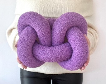May include: A large, purple, knotted pillow. The pillow is made of a soft, fuzzy fabric and is shaped like a figure eight.