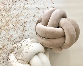 May include: Two knotted throw pillows, one in beige and one in white. The pillows are made of a soft, plush fabric and have a simple, modern design.