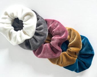 Può includere: Cinque scrunchies in diversi colori: bianco, grigio, rosa, oro e blu. Gli scrunchies sono realizzati in tessuto morbido e vellutato.
