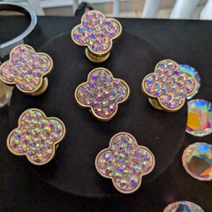 May include: Six gold-toned cabinet knobs with a four-leaf clover design. Each knob is covered in iridescent rhinestones.