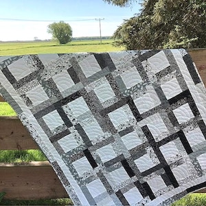 Könnte beinhalten: Eine schwarz-weiße Quiltdecke mit geometrischem Muster. Die Decke besteht aus Quadraten und Rechtecken, und der Stoff hat ein Blumenmuster. Die Decke hängt an einem Holzzaun.