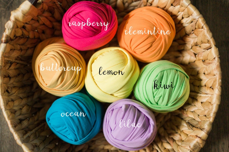 May include: A wicker basket filled with colorful fabric rolls, labeled with names like "raspberry", "clementine", "buttercup", "lemon", "kiwi", "ocean", "lilac".