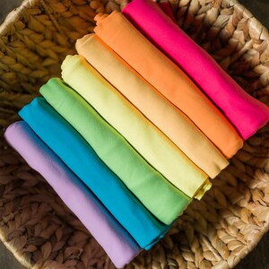 May include: A stack of colorful fabric swatches in a woven basket. The swatches are arranged in a rainbow pattern, starting with purple and ending with red.