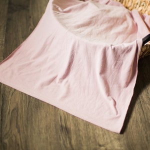 May include: A pale pink fabric backdrop draped over a woven basket. The fabric is smooth and wrinkle-free, creating a soft and neutral background for photography.