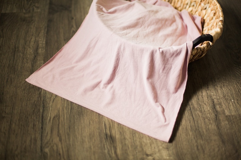 May include: A pale pink fabric backdrop draped over a woven basket. The fabric is smooth and wrinkle-free, creating a soft and neutral background for photography.