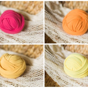May include: Four fabric rolls in different colors: pink, orange, yellow, and light yellow. The rolls are arranged in a grid pattern on a white crocheted surface.