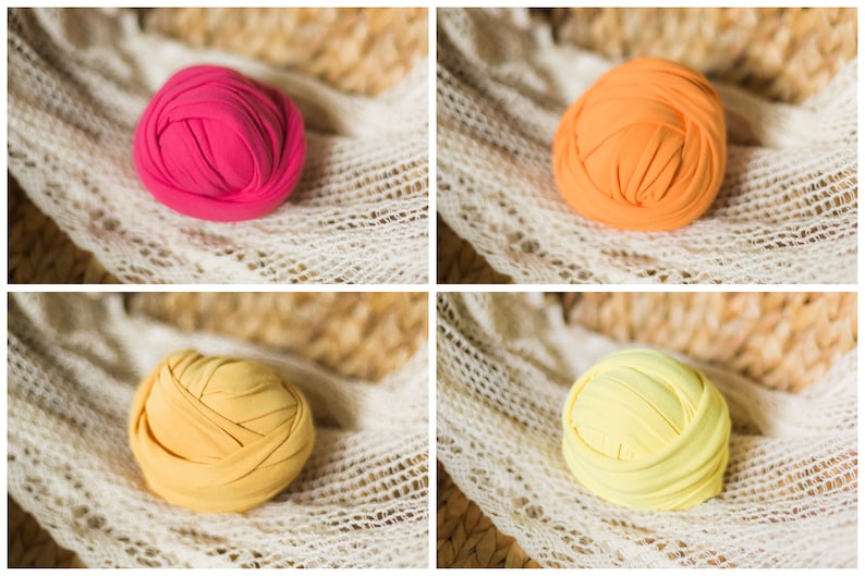 May include: Four fabric rolls in different colors: pink, orange, yellow, and light yellow. The rolls are arranged in a grid pattern on a white crocheted surface.