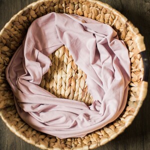 May include: A woven wicker basket with a light pink fabric lining. The basket is round and has two black handles.