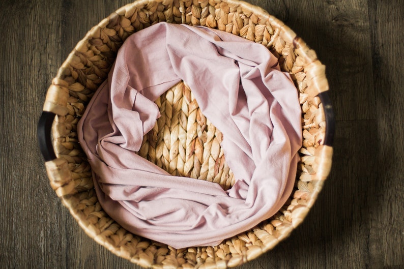 May include: A woven wicker basket with a light pink fabric lining. The basket is round and has two black handles.