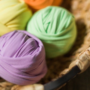 May include: A basket filled with colorful fabric balls. The balls are made of soft, stretchy fabric and are arranged in a rainbow pattern. The basket is made of woven wicker and has a dark brown handle.