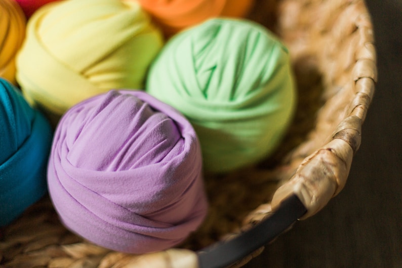 May include: A basket filled with colorful fabric balls. The balls are made of soft, stretchy fabric and are arranged in a rainbow pattern. The basket is made of woven wicker and has a dark brown handle.