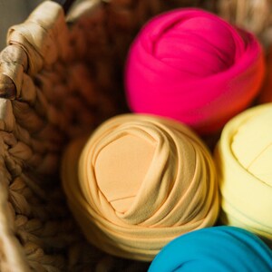 May include: A wicker basket filled with colorful fabric rolls. The rolls are in shades of pink, orange, yellow, blue, and purple. The fabric is soft and stretchy, perfect for newborn photography props.