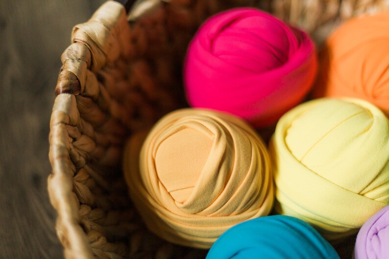 May include: A wicker basket filled with colorful fabric rolls. The rolls are in shades of pink, orange, yellow, blue, and purple. The fabric is soft and stretchy, perfect for newborn photography props.
