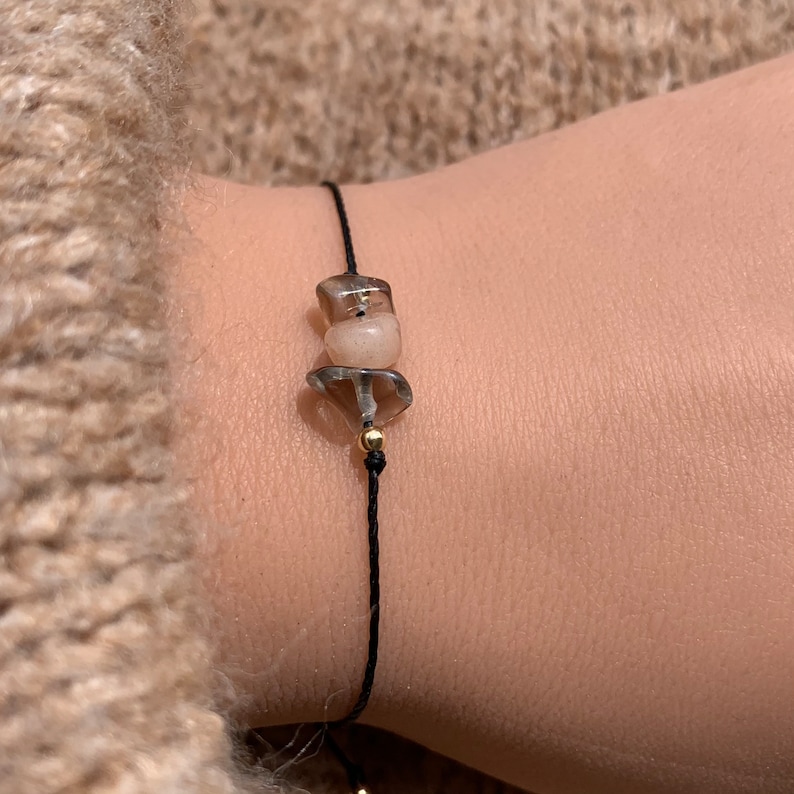 May include: A simple bracelet with a black cord and two clear, faceted gemstone beads. The beads are a light brown and a darker brown.