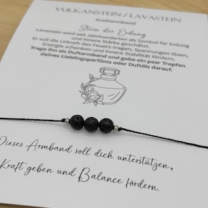Può includere: Un braccialetto in pietra lavica nera con tre perline rotonde e porose infilate su un cordino nero. Il braccialetto è presentato su una carta bianca con testo in tedesco e un'illustrazione di un flacone di profumo.