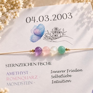 Könnte beinhalten: Ein Perlenarmband mit vier runden Edelsteinen in Violett, Rosa, Weiß und Grün, getrennt durch kleine goldfarbene Perlen auf einer dünnen Schnur. Das Armband liegt auf einer Karte mit dem Datum 04.03.2003, einem blauen Schmetterling und Text.