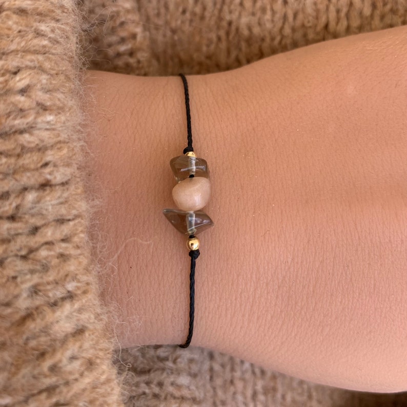 May include: A simple bracelet with a black cord and two brown gemstone beads. The beads are faceted and have a light brown color.