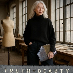 May include: A woman with grey hair in a black turtleneck and dark jeans, holding a tweed clutch. The clutch combines blue, green, and brown fabrics. The image features the text "TRUTH + BEAUTY" at the bottom, suggesting a fashion or lifestyle theme.