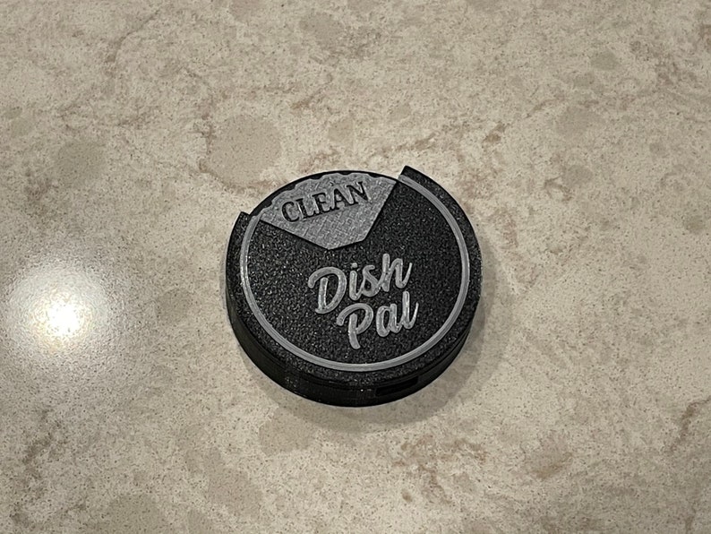 Puede incluir: Un "Dish Pal" redondo negro y gris con las palabras "Dish Pal" y "Clean" en &eacute;l.