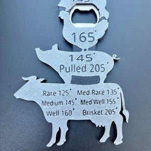 May include: A silver metal meat thermometer shaped like a cow, pig, and a bottle opener. The thermometer has different temperatures for different types of meat, including rare, medium rare, medium, medium well, well, pulled pork, and brisket.