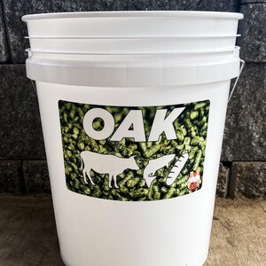 Pu&ograve; includere: Un secchio di plastica bianco con un manico in metallo. Il secchio ha un'etichetta con la parola "OAK" in grandi lettere bianche, insieme a illustrazioni di una mucca, un pesce e un pollo. Lo sfondo dell'etichetta &egrave; verde.