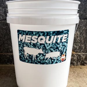 Pu&ograve; includere: Un secchio di plastica bianco con coperchio, con un'etichetta con la scritta "MESQUITE" in bianco. L'etichetta mostra sagome di una mucca e di un maiale, su uno sfondo di pellet blu scuro.