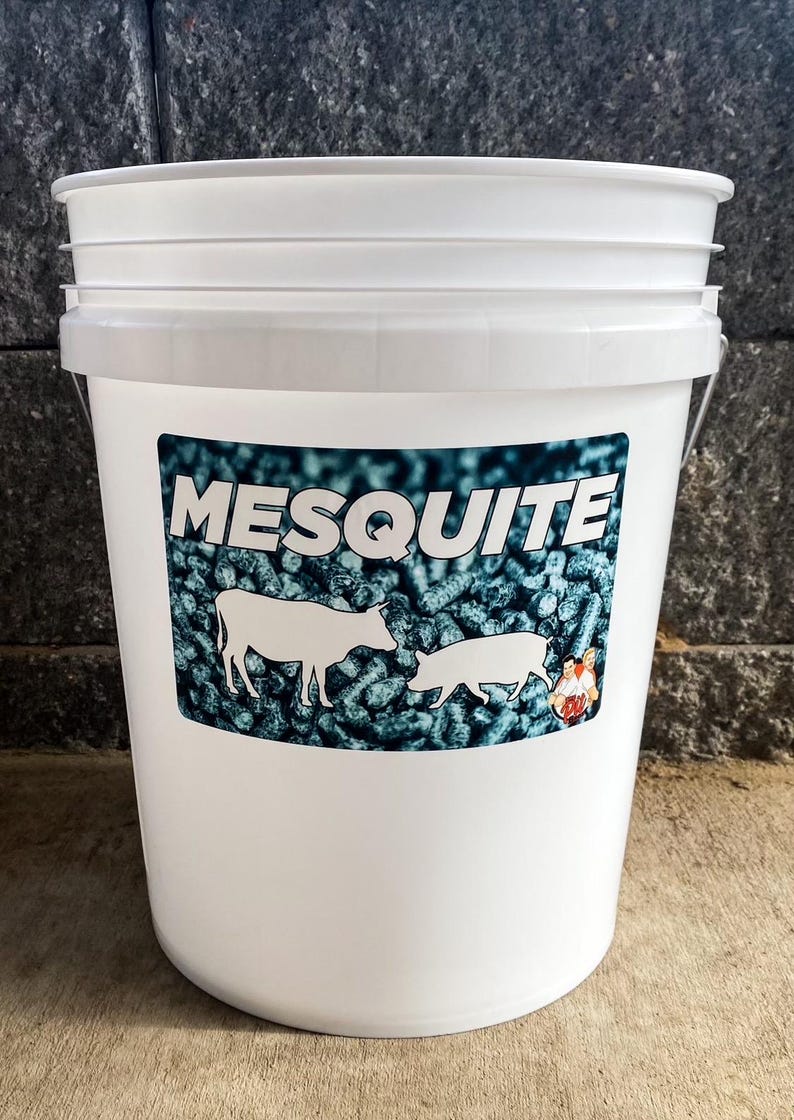 Pu&ograve; includere: Un secchio di plastica bianco con coperchio, con un'etichetta con la scritta "MESQUITE" in bianco. L'etichetta mostra sagome di una mucca e di un maiale, su uno sfondo di pellet blu scuro.