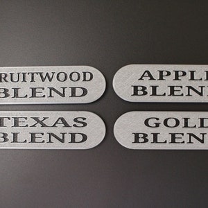 May include: Four silver metal labels with black text. The labels read "Fruitwood Blend", "Apple Blend", "Texas Blend", and "Gold Blend".