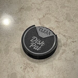 Puede incluir: Un "Dish Pal" redondo de color negro y gris con las palabras "Dish Pal" y "Clean" en &eacute;l.