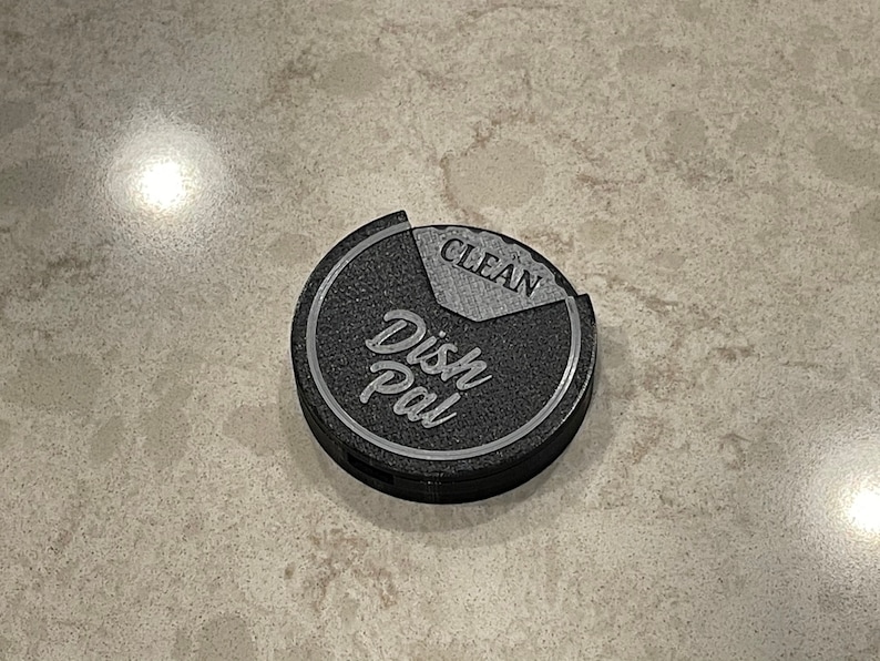 Puede incluir: Un "Dish Pal" redondo de color negro y gris con las palabras "Dish Pal" y "Clean" en &eacute;l.
