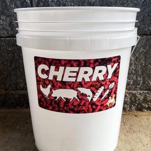 Pu&ograve; includere: Un secchio di plastica bianco con un'etichetta rossa e bianca. L'etichetta recita "CHERRY" a grandi lettere bianche. Sagome di pollo, maiale, pesce e verdure sono anche sull'etichetta. Il secchio ha un manico in metallo.