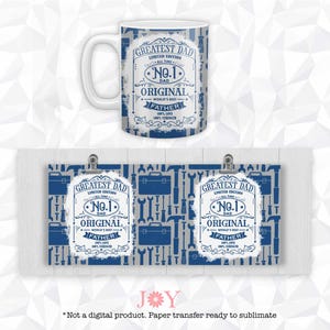 May include: White ceramic mug and two paper transfers with a blue and white design. The mug and transfers feature the text "GREATEST DAD" and "No. 1 DAD". The background has a pattern of tools. The transfers are held by silver clips.