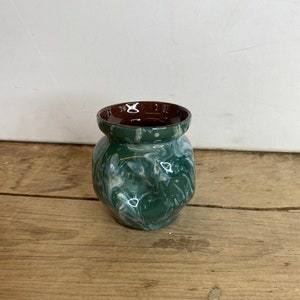 May include: A small, handcrafted ceramic vase with a dark green and white marbled design. The interior of the vase is a rich brown colour. The vase has a rounded body and a slightly flared rim, ideal for displaying small flowers or decorative items.