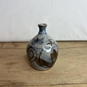 May include: A small, hand-painted ceramic vase with a blue and brown glaze. The vase has a rounded body and a narrow neck.